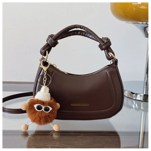 Detail of dark brown crescent handbag with knotted handle and plush charm on glass table