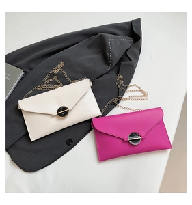 Détail de pochettes enveloppes crème et rose avec chaînes sur une veste de costume grise