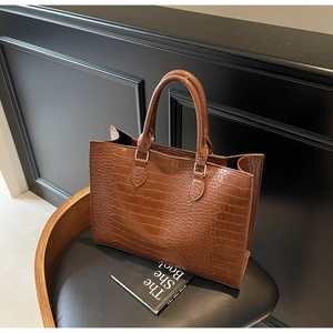 Detailed view of brown crocodile texture and metal hardware on large leather tote bag