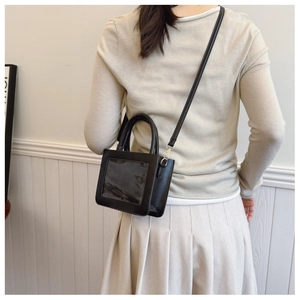 Detail view of black PVC ita bag showing the transparent window and crossbody strap on model