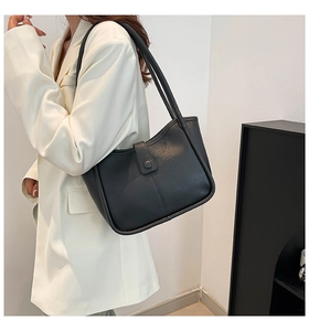Close-up of black leather shoulder bag with buckle flap closure on white blazer