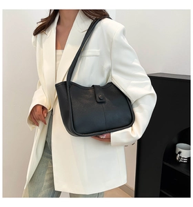 Detail of minimalist black leather tote bag with round buckle and extended shoulder strap