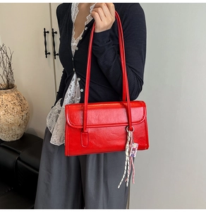 Close-up of vibrant red leather shoulder bag with decorative woven pendant and tag