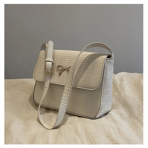 Détail de la texture cuir crocodile avec nœud doré métallique sur le sac à bandoulière