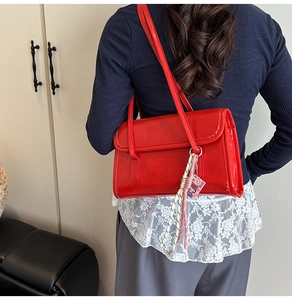 Chic red glossy shoulder bag with woven pendant charm shown on model's shoulder