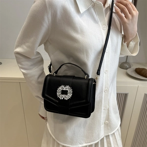 Elegant black leather handbag with luxury crystal buckle and top handle worn by a model