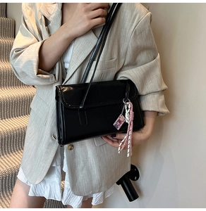 Détail du sac sous le bras en cuir noir brillant avec pendentif rose sur mannequin