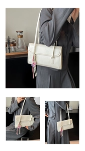 Detail of a minimalist cream rectangular flap shoulder bag with a decorative purple charm