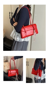 Close-up of red glossy leather shoulder bag with chic woven tassel and cartoon charm