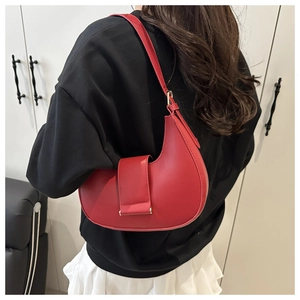 Red matte crescent shoulder bag with belt buckle detail shown on a model's shoulder