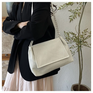 Detailed view of cream textured tote bag with chain strap on model in elegant suit