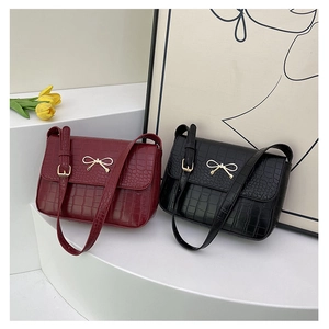 Détail de sacs bandoulière aspect crocodile rouge et noir avec boucles nœud doré