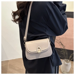 Detail of beige faux leather saddle bag featuring a gold horseshoe clasp and shoulder strap