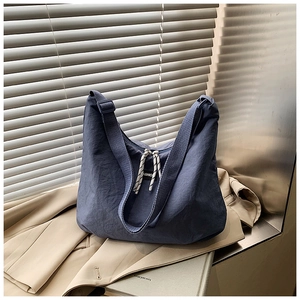 Detail of navy nylon crescent bag with wide strap and rope zipper on a beige blazer