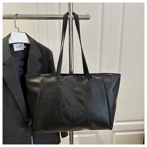 Close-up of the embossed logo on a black large capacity tote bag made of textured faux leather