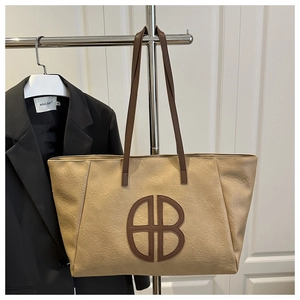 Detail of a large beige leather tote bag with a dark brown round logo and wide straps