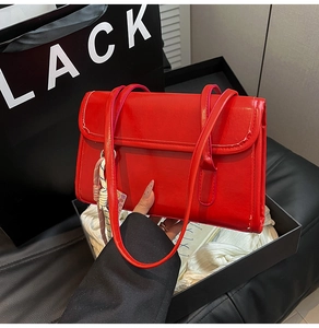 Detailed view of glossy red rectangle underarm bag with woven pendant in luxury packaging