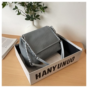 Detail of grey knitted crossbody bag with silver chain and blue leather strap in a box