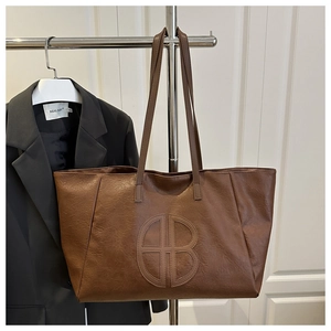 Detailed close-up of brown tote bag with embossed circular logo and lychee grain texture