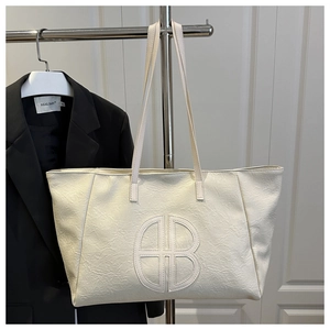 Detail of cream large tote bag featuring stitched AB logo and premium leather texture