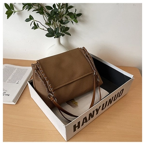 Detail of brown corduroy shoulder bag with metal chain strap in minimalist home setting