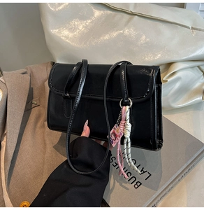 Close-up of black faux leather shoulder bag with colorful woven rope and pink pendant