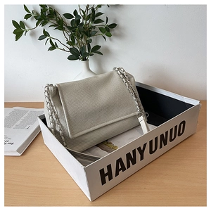 Detail of beige textured fabric shoulder bag with silver chain strap inside a white box