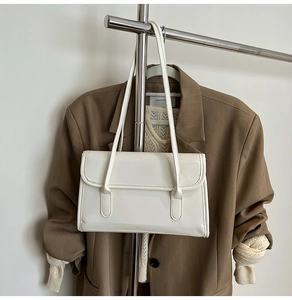 White rectangular minimalist shoulder bag with flap closure hanging on a metal rack