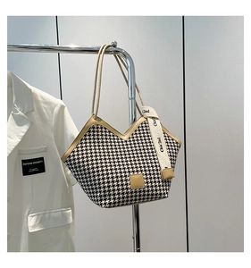 Detail of houndstooth tote bag with V-cut edge and brown leather handles on a hanger