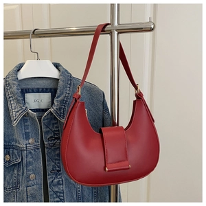 Red half-moon underarm bag with gold metal buckle detail against denim jacket backdrop