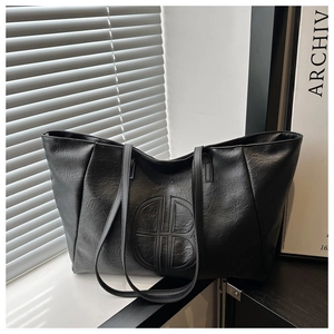 Detail of black PU leather tote bag featuring a circular stitched logo and slim shoulder straps