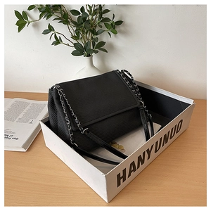 Detail of black twill crossbody bag with silver metal chain strap in a lifestyle setting