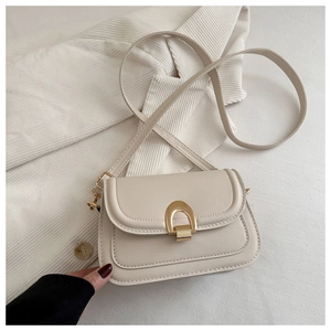 Detailed close-up of cream leather saddle bag with shiny gold horseshoe metal clasp