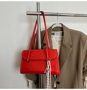 Detail of red glossy leather shoulder bag with matching strap and cute charm accessory