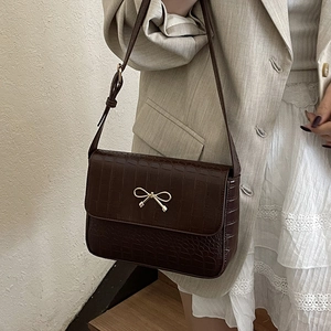 Sac à bandoulière marron foncé motif crocodile avec boucle nœud doré sur blazer beige