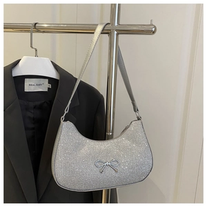 Detailed close-up of a silver crescent handbag featuring a metallic bow and sparkling sequins