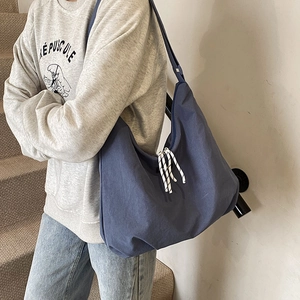 Minimalist large blue nylon hobo tote bag with striped knot zipper on a crossbody model