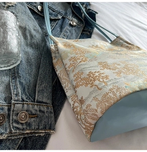 Detail of floral jacquard tote bag featuring gold mountain landscape and blue leather straps