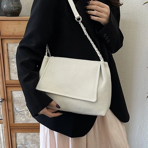 White textured shoulder bag with silver chain strap shown on a model in a minimalist style