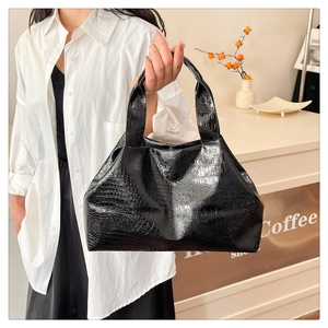 Close-up of black glossy crocodile pattern tote bag held by model in a cafe setting