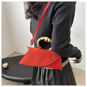 Detail of red suede bag with asymmetrical shape and sculptural gold metal handle