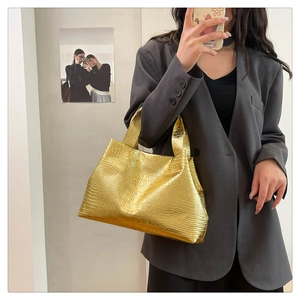 Macro shot of metallic gold tote bag with embossed crocodile texture and top handle