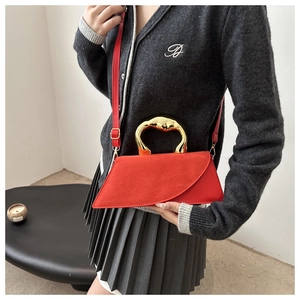Close-up of modern red handbag featuring unique irregular gold wave-shaped metal handle