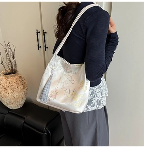 Close-up of traditional floral embroidery and silver tassel on off-white satin tote bag