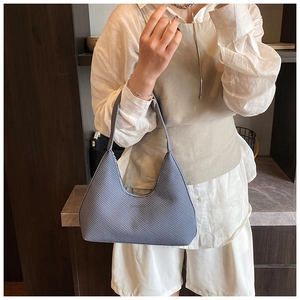 Detail of grey-blue woven texture shoulder bag worn by model in an elegant interior