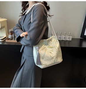 Detail of beige satin tote bag featuring green bamboo embroidery and grey tassel accent