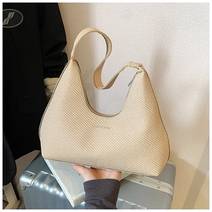 Détail du sac hobo tissé beige montrant la texture paille et le zip sur une valise