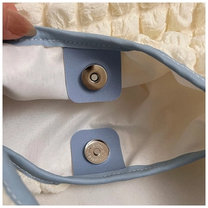 Detail of magnetic metal clasp on creamy ruched fabric tote bag with light blue leather trim
