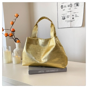 Detailed view of the gold crocodile embossed texture and wide handle on this tote bag