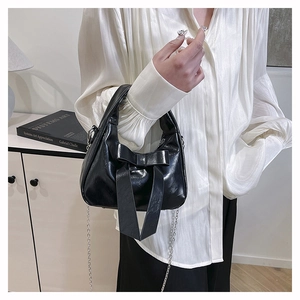 Detail of a black glossy handbag with a large leather bow and silver chain strap